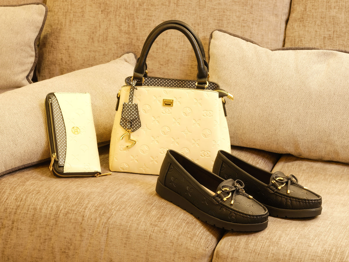 Elegant black moccasins with gold accents paired with a stylish cream handbag and matching wallet on a beige sofa.